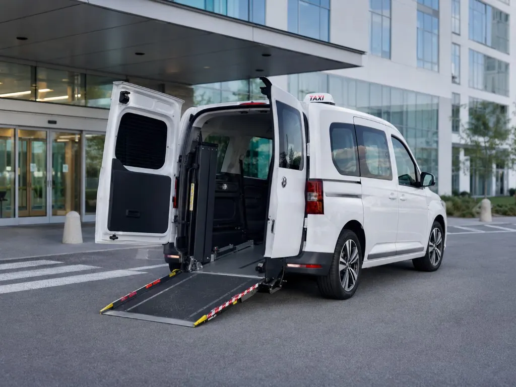 Taxi TPMR Volkswagen Caddy blanc Tara Taxi, rampe ouverte devant l'entrée d'un hôpital